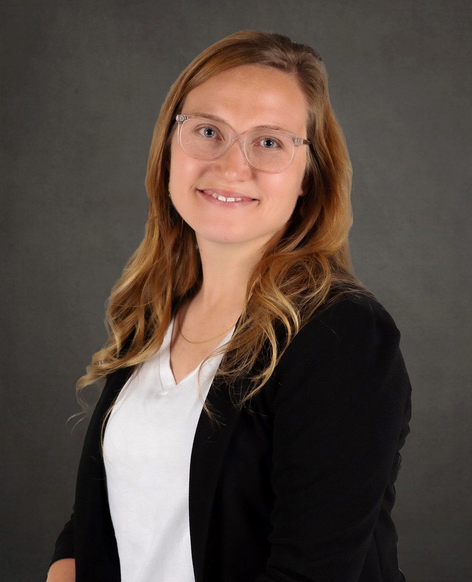 A woman wearing glasses and a black jacket is smiling for the camera.