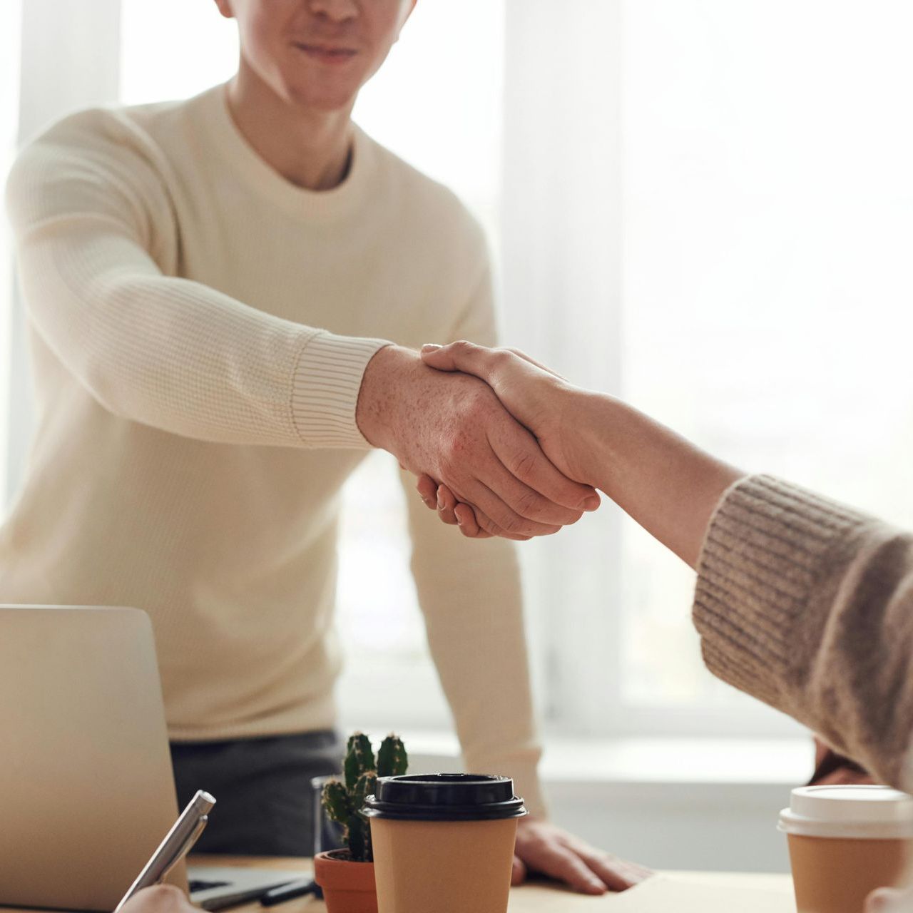A man is shaking hands with a woman in front of a laptop.