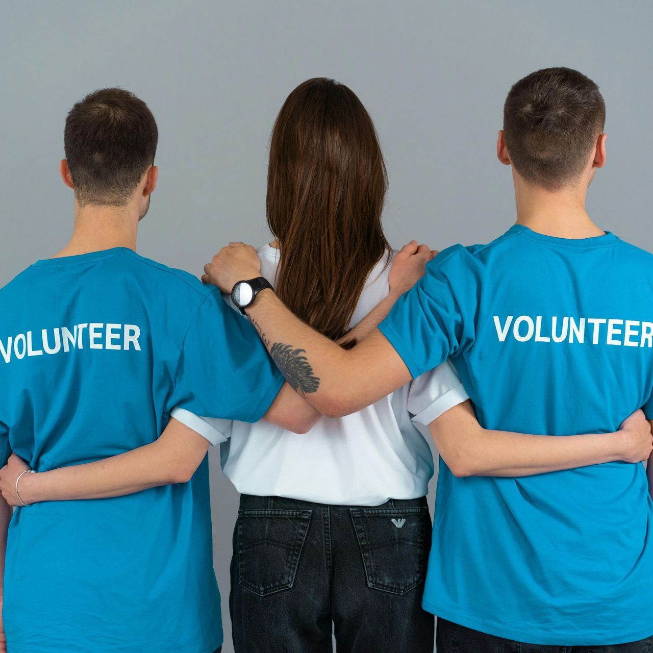 Three people wearing blue volunteer shirts are hugging each other