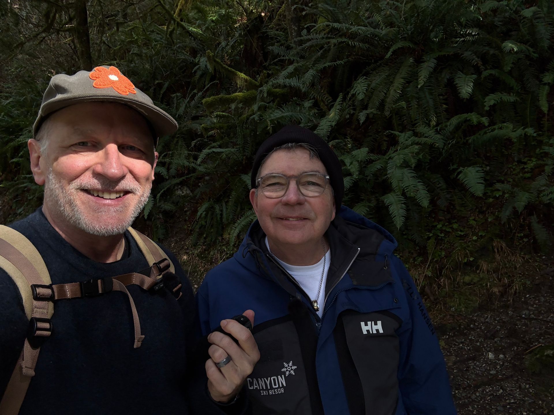 Two people smiling for a selfie on a trail surrounded by lush green ferns.