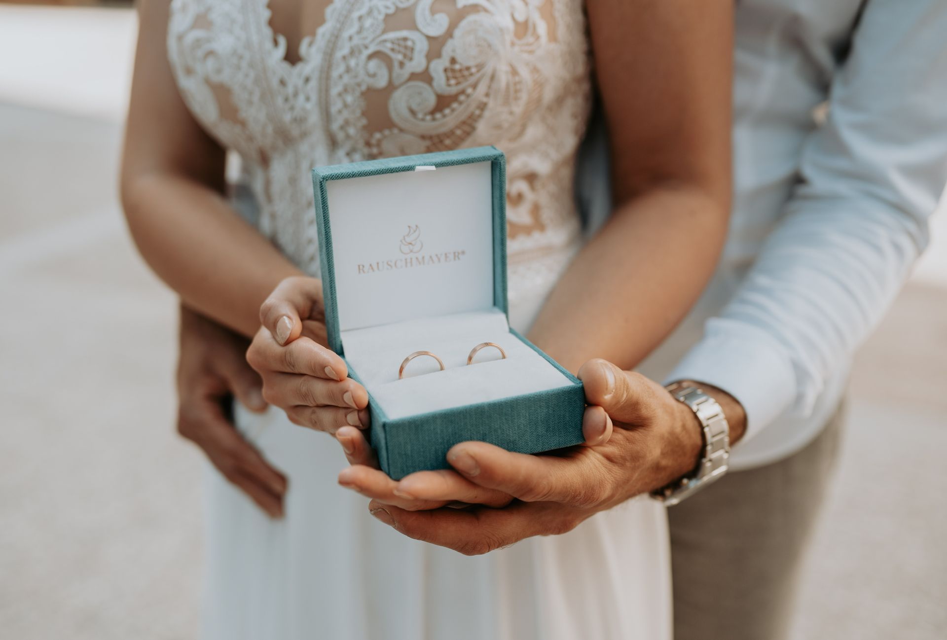 Eine Braut und ein Bräutigam halten eine Schachtel mit Eheringen darin.