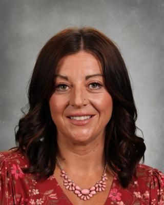 A woman wearing a white shirt and a necklace is smiling for the camera.