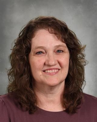 A woman in a floral shirt and a black jacket is smiling for the camera.