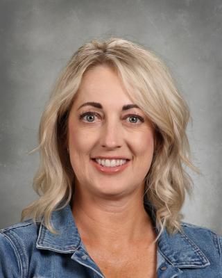 A woman wearing glasses and a blue shirt is smiling for the camera.