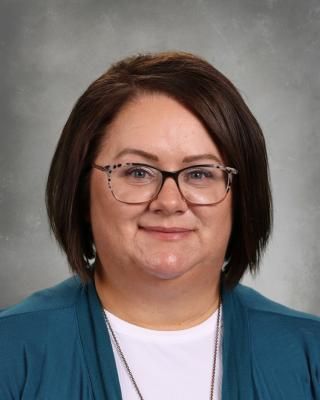 A woman wearing glasses and a blue sweater is smiling for the camera.