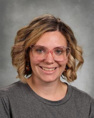 A woman wearing glasses and a blue shirt is smiling for the camera.