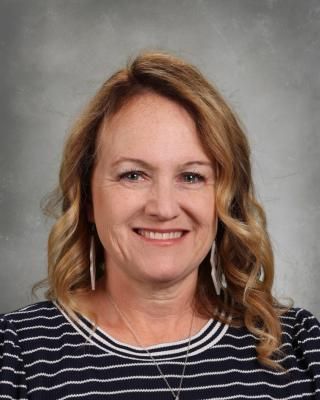 A woman in a white shirt with flowers on it is smiling for the camera.
