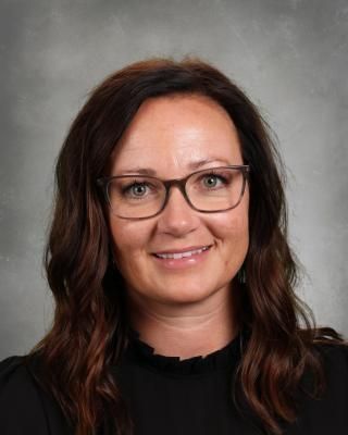 A woman wearing glasses and earrings is smiling for a picture.