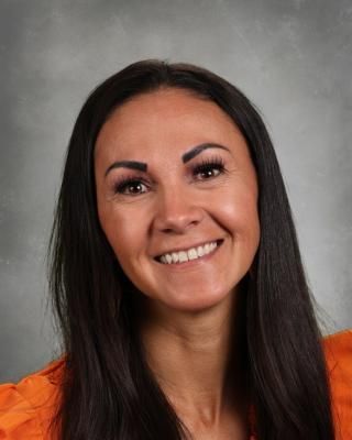 A woman with long hair and red earrings is smiling for a picture.