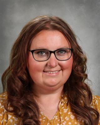 A woman wearing glasses and a yellow shirt is smiling for the camera.