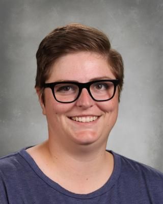A woman wearing glasses and a black sweater is smiling for the camera.