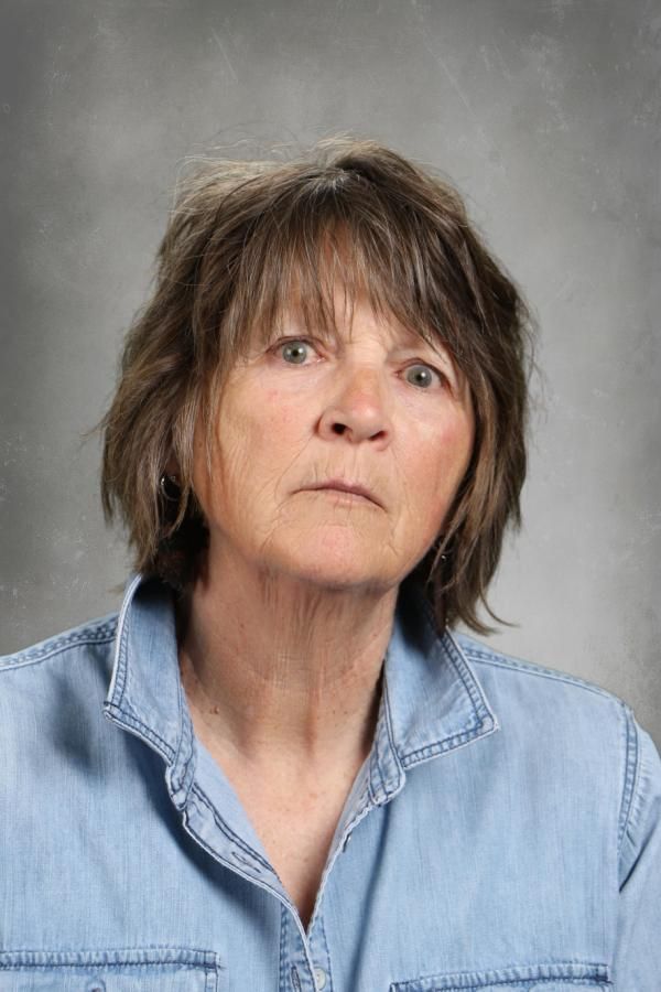 A woman in a blue denim shirt is looking at the camera.