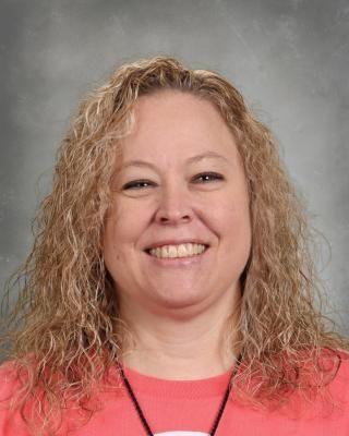 A woman is wearing a purple tie dye shirt and smiling for the camera.