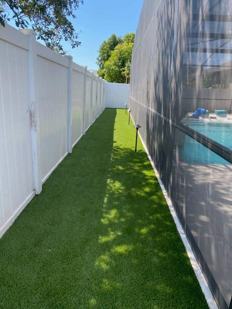 A white fence surrounds a lush green lawn next to a pool.
