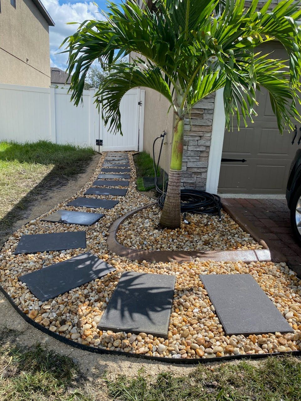 A walkway leading to a garage with a palm tree in the middle.