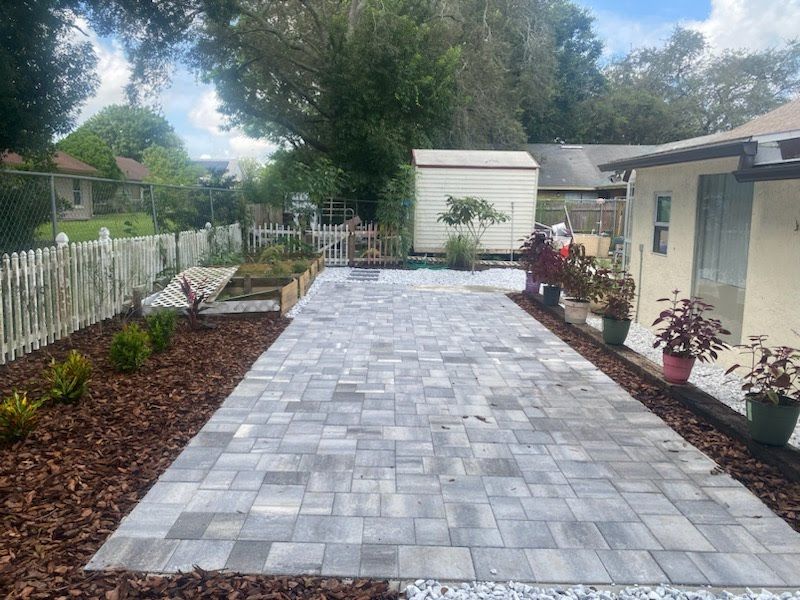 A brick driveway leading to a house with a white picket fence.