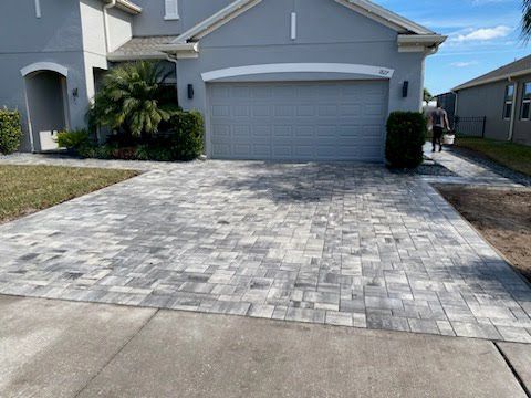 A man is walking down a brick driveway in front of a house.