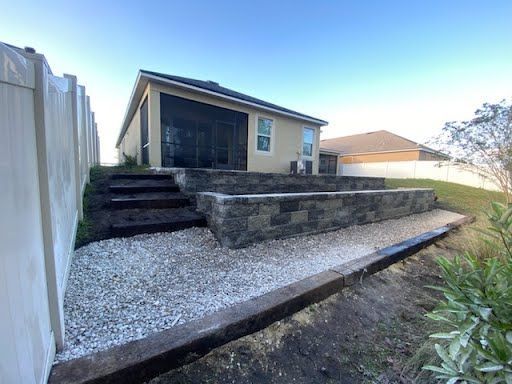 A house with a screened in porch and a stone wall in the backyard.