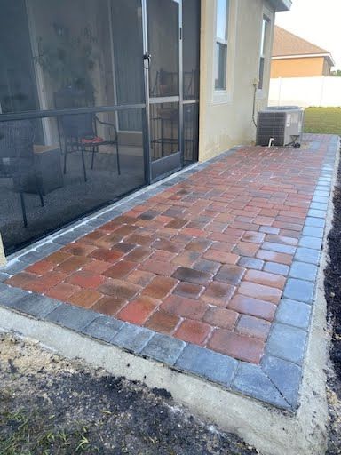 A brick patio with a screened in porch next to a house.