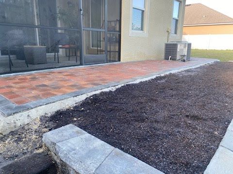 A brick patio is being built in the backyard of a house.