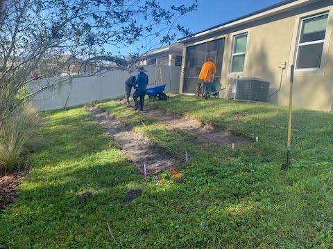 Two men are working on a lawn in front of a house.