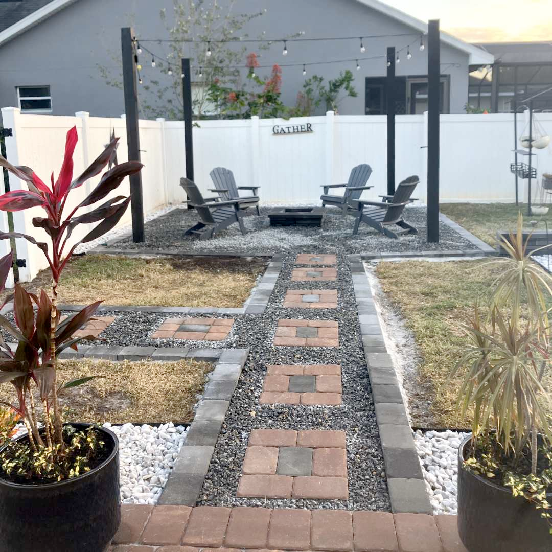 A brick walkway leads to a patio with chairs and a fire pit