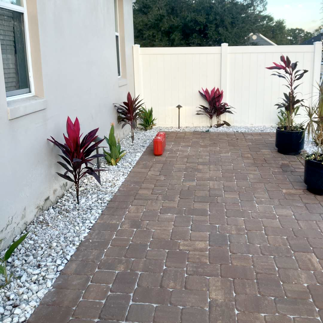 A brick walkway with plants and rocks along the side of a house