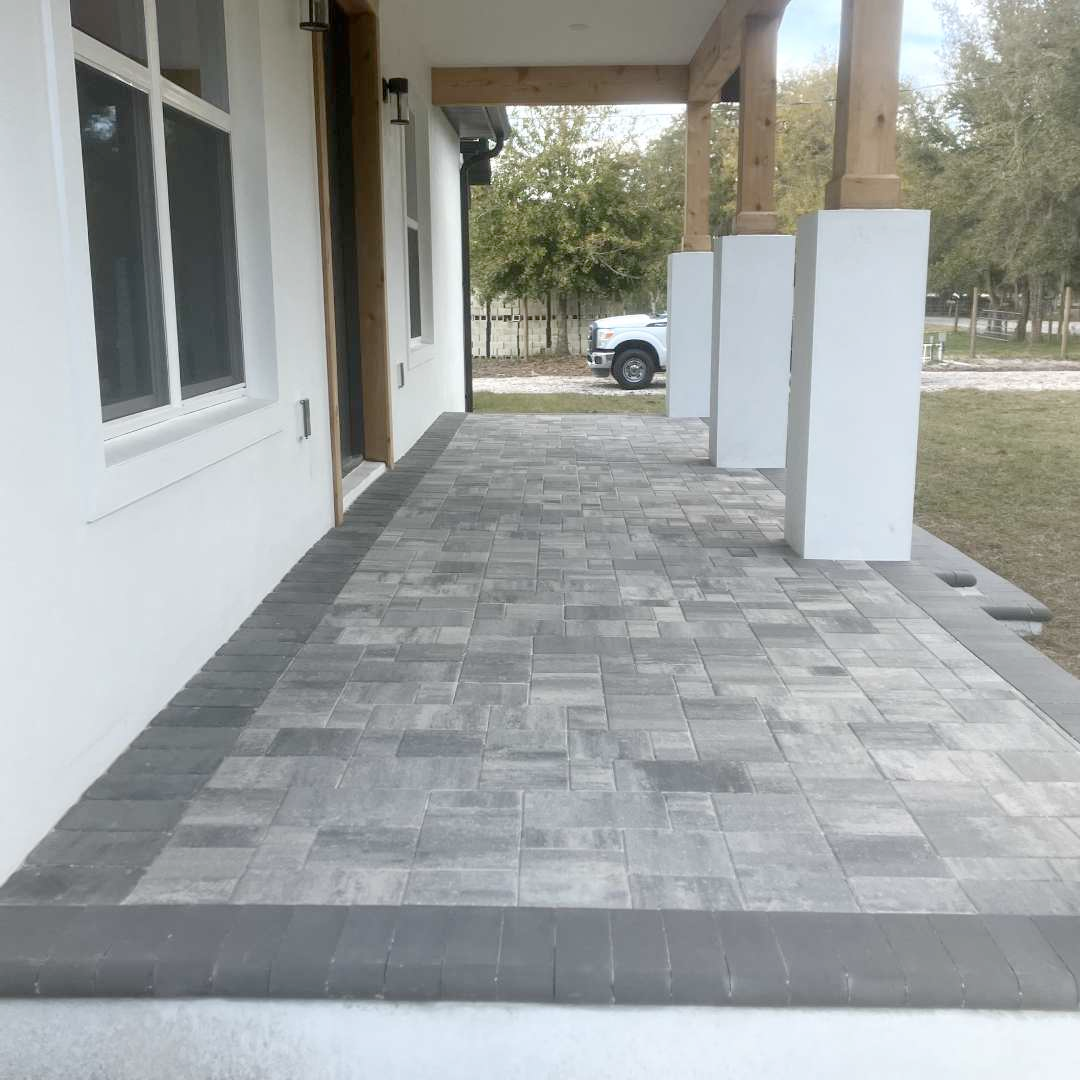 A brick walkway leading to a white house with a truck parked in the background.
