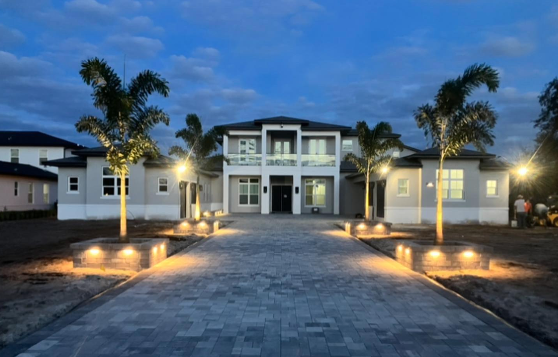A large house is lit up at night with palm trees in front of it