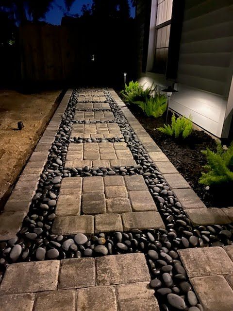 A stone walkway leading to a house is lit up at night.