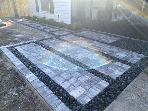 A brick walkway with black rocks in the middle is being built in front of a house.