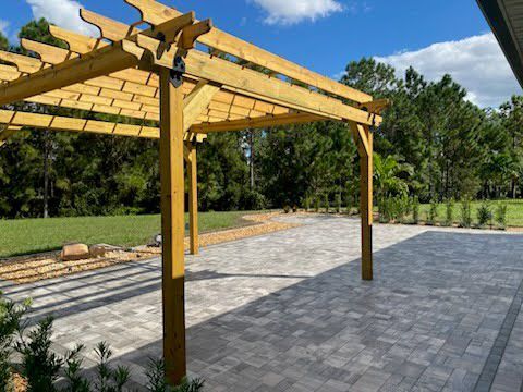 Wooden pergola over a brick patio in a backyard with green grass and trees.
