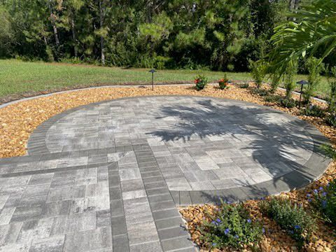 Circular paved patio with brick border, surrounded by brown gravel and landscaping.