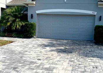 A gray garage door is sitting next to a brick driveway.