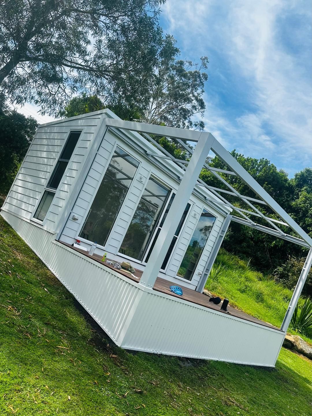 White greenhouse-style structure on a grassy hillside. Features large glass windows and an open roof frame.