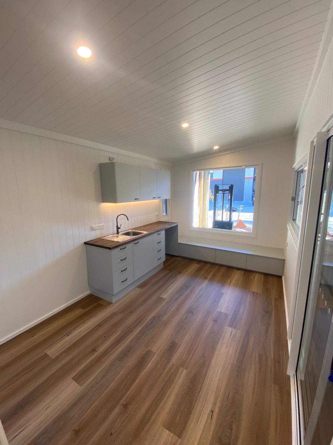 A modern kitchen with light gray cabinets, a wood countertop, and wood-look flooring under a white paneled ceiling.