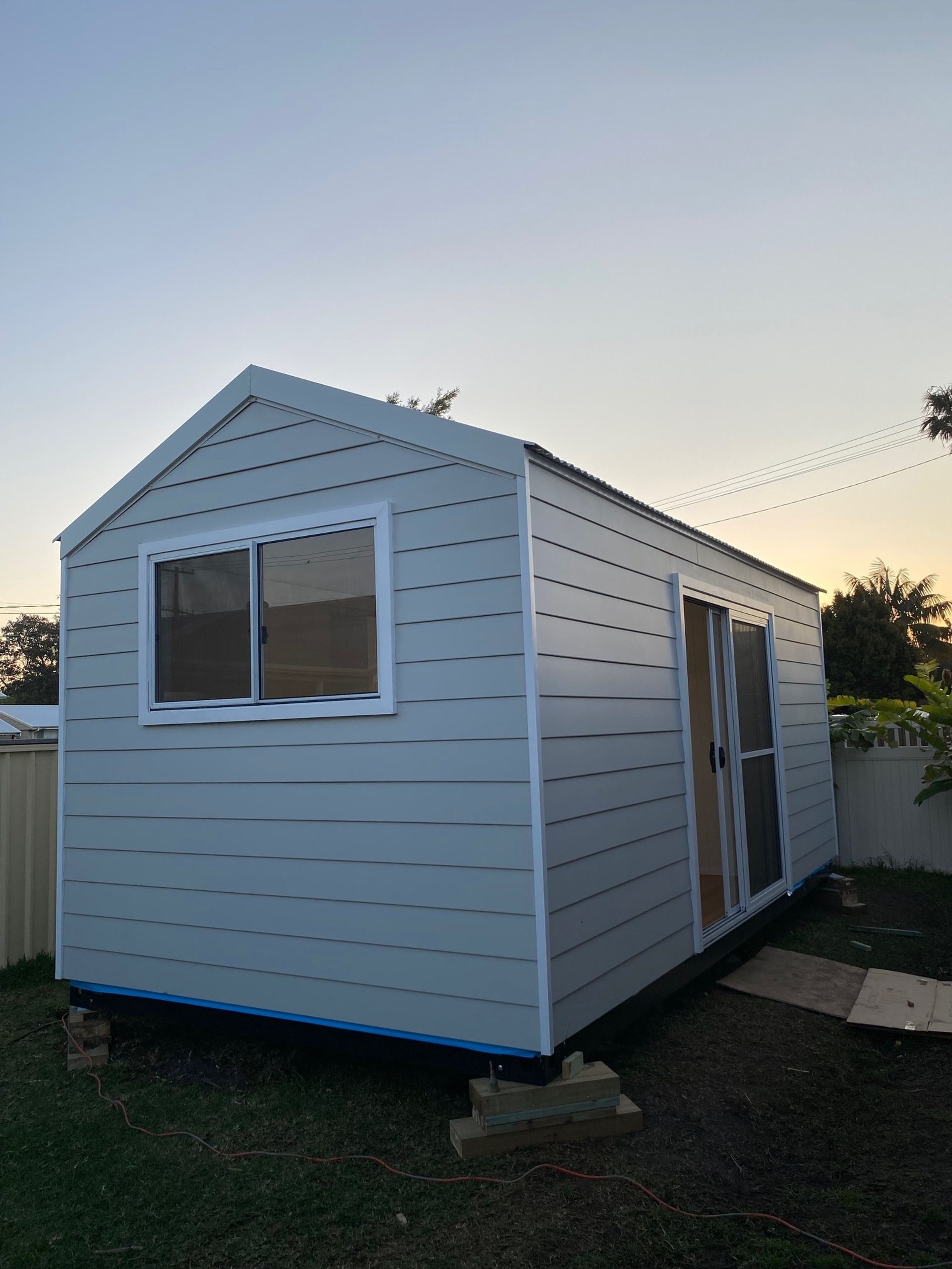 Light blue shed with white trim, window, and sliding door on a grassy lawn under a dusky sky.