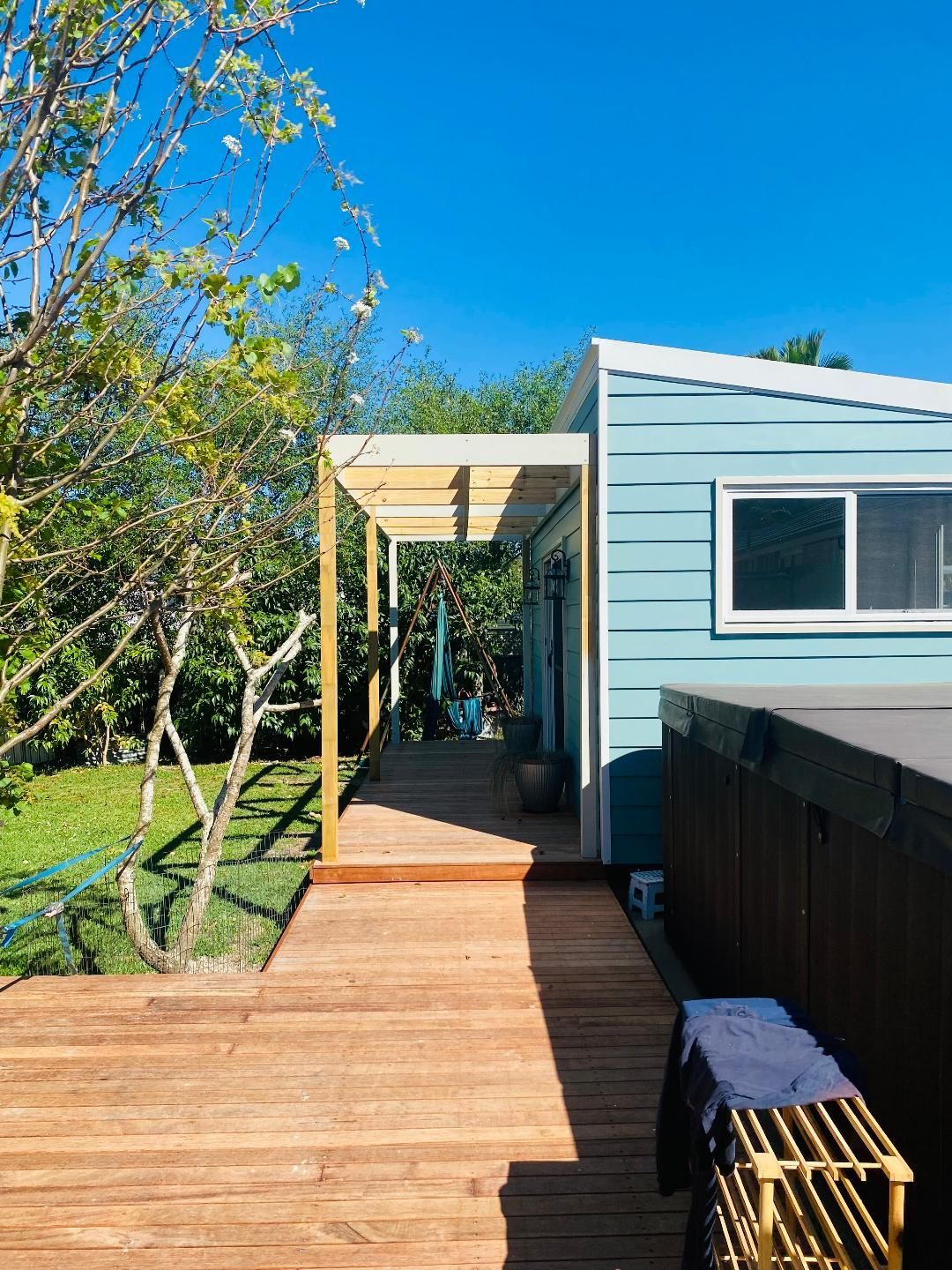 Wooden walkway leading to a light blue cabin with a hot tub on a sunny day.