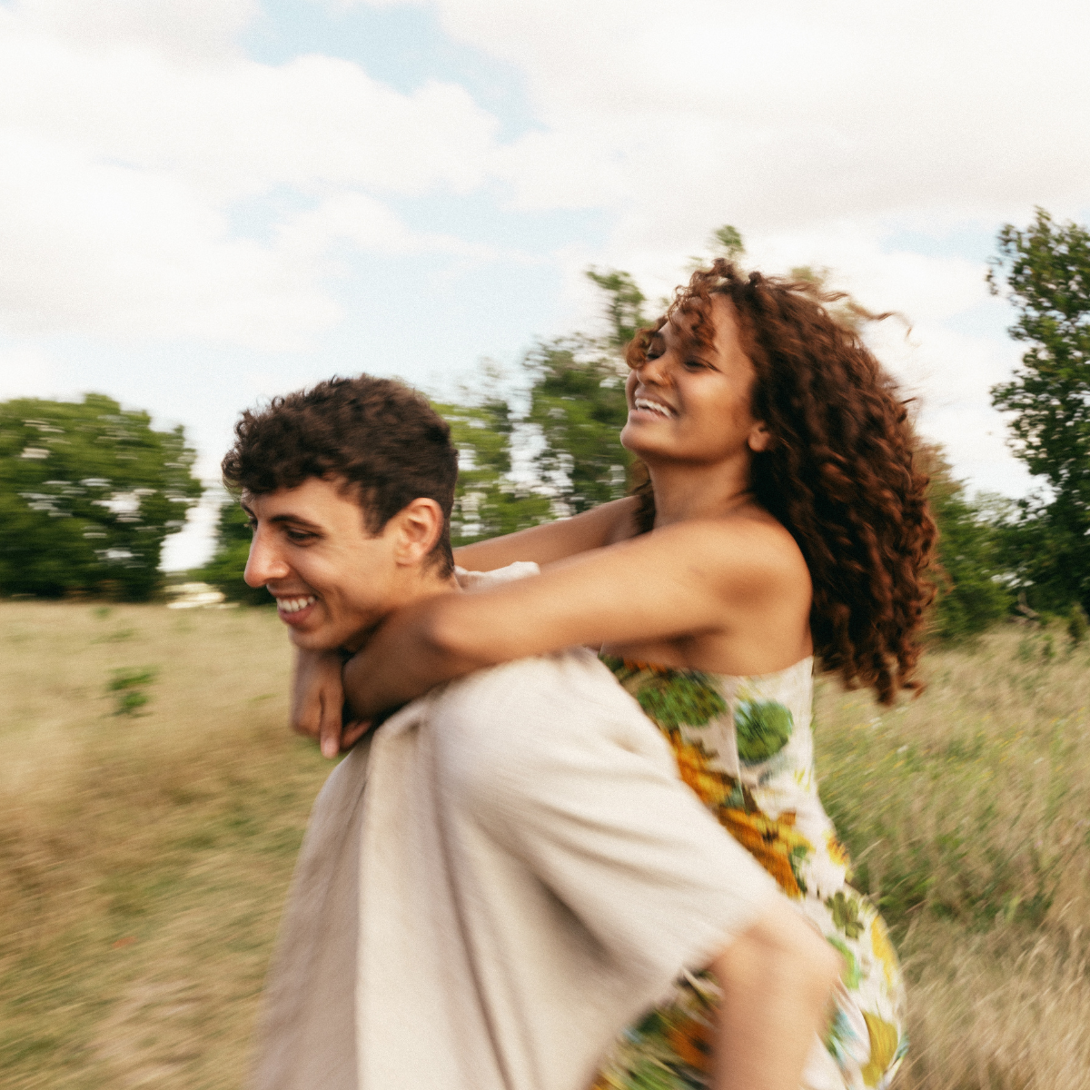 Man carrying woman on his back, both smiling in a grassy field.