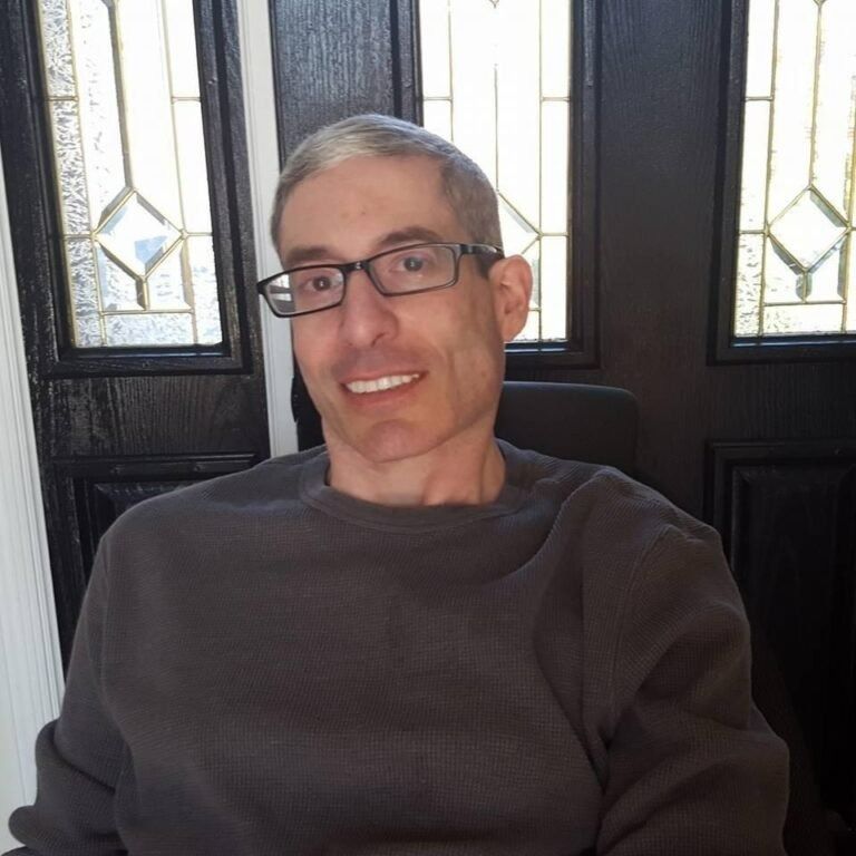 A man wearing glasses is sitting in front of a door