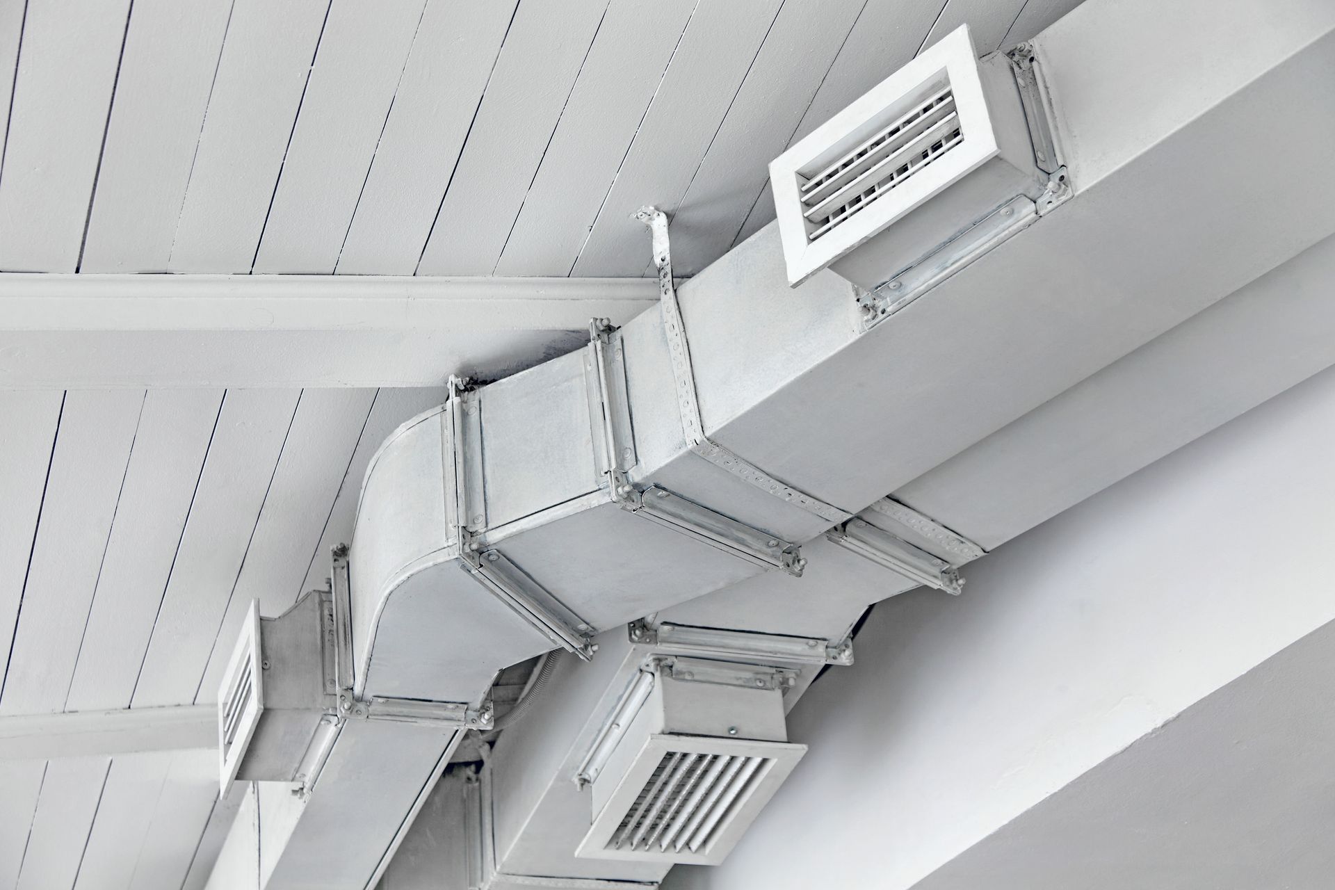 White air ducts attached to a white ceiling and wall with air vents.