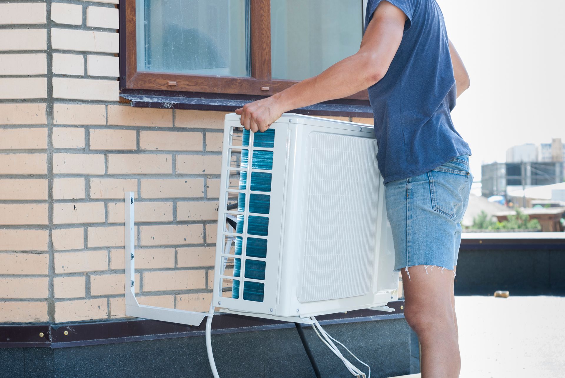 Person installing an air conditioning unit outside a brick building.