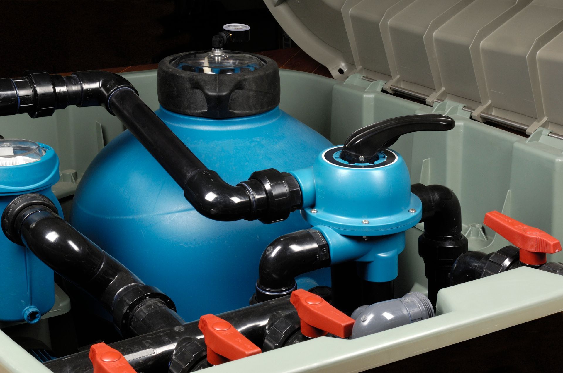 Blue and black pool filter system inside a green box with red valves and black piping.