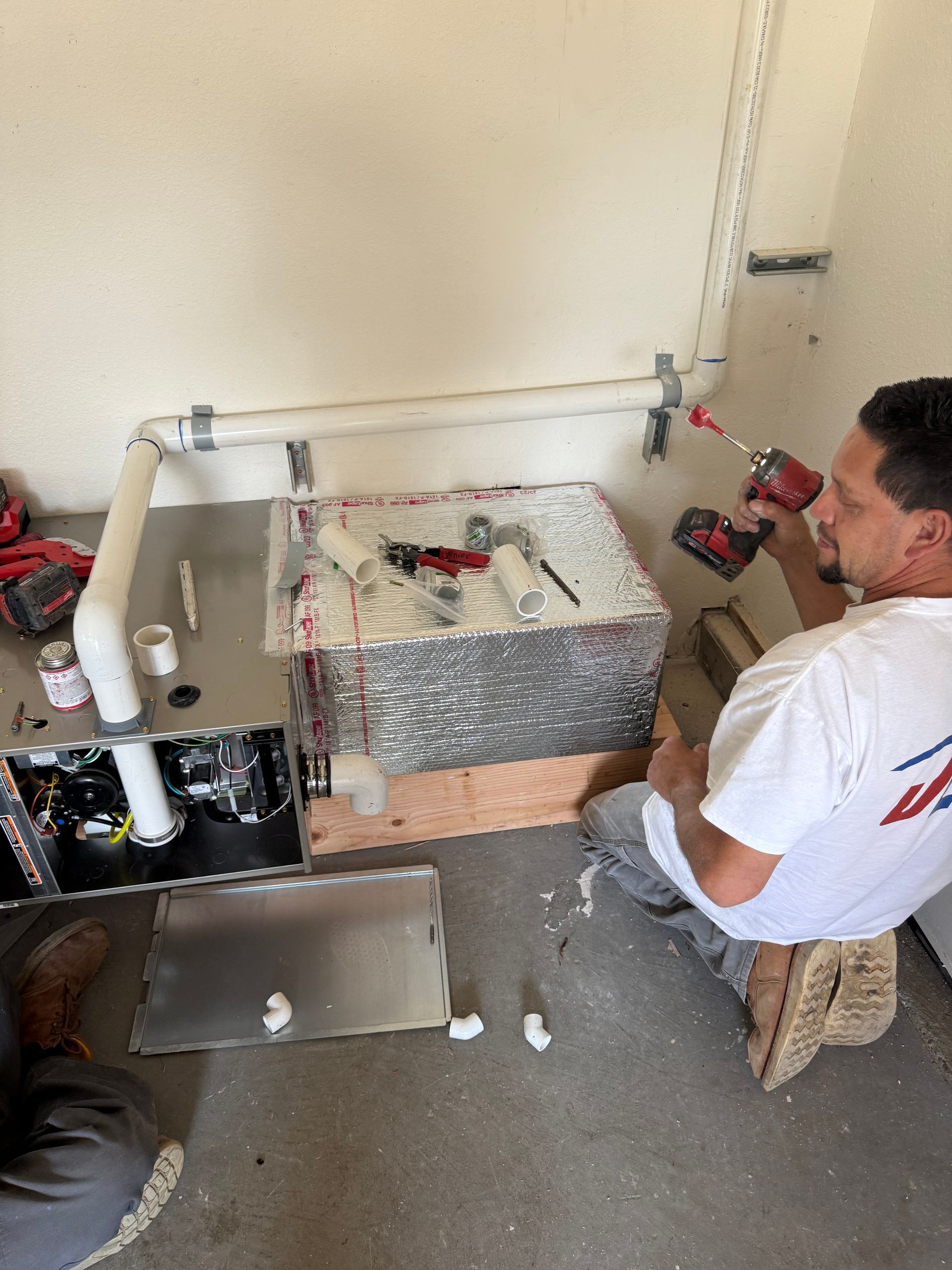 Worker black gloves working on copper pipes with a wrench and screwdriver.