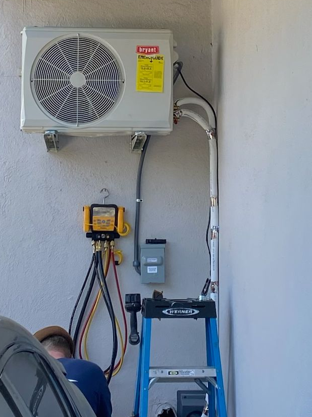 HVAC technician in yellow hardhat inspecting an indoor air conditioning unit, on a wall.