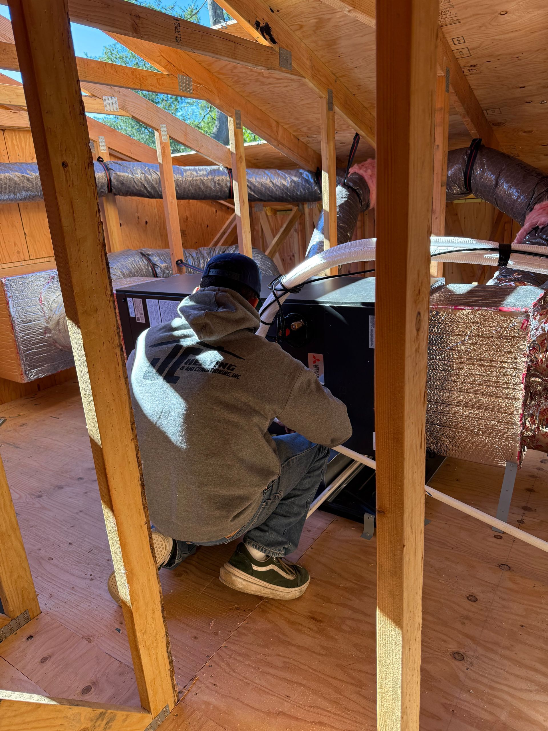 Man in overalls, inspecting a red fire alarm control panel. Holds a red hard hat, indoors.
