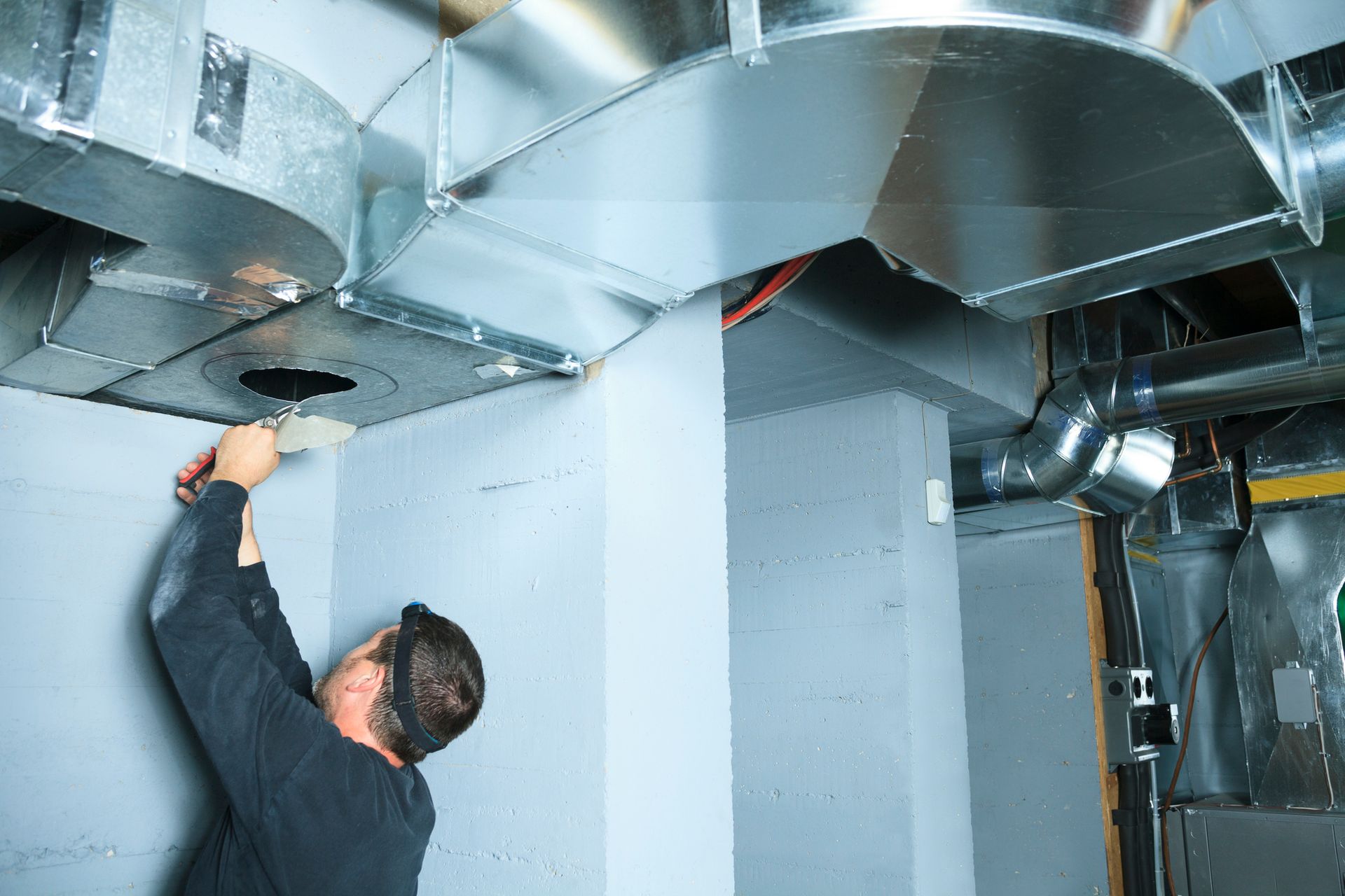 Person working on HVAC ductwork in a basement setting.