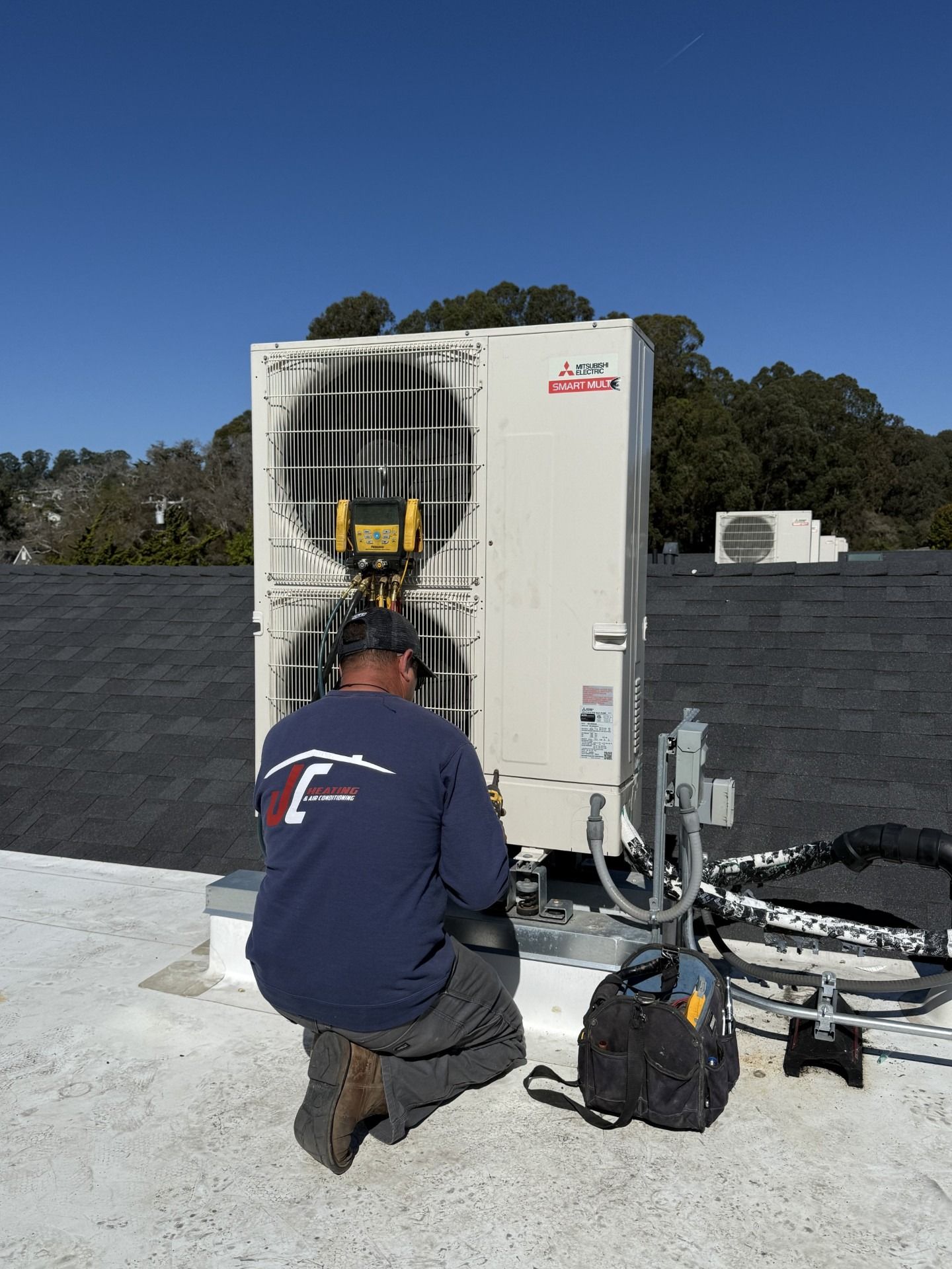 HVAC technician in yellow hard hat working on outdoor air conditioner unit on a building.