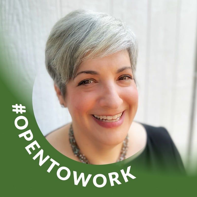 Woman with short gray hair smiles, wearing a necklace. Green 