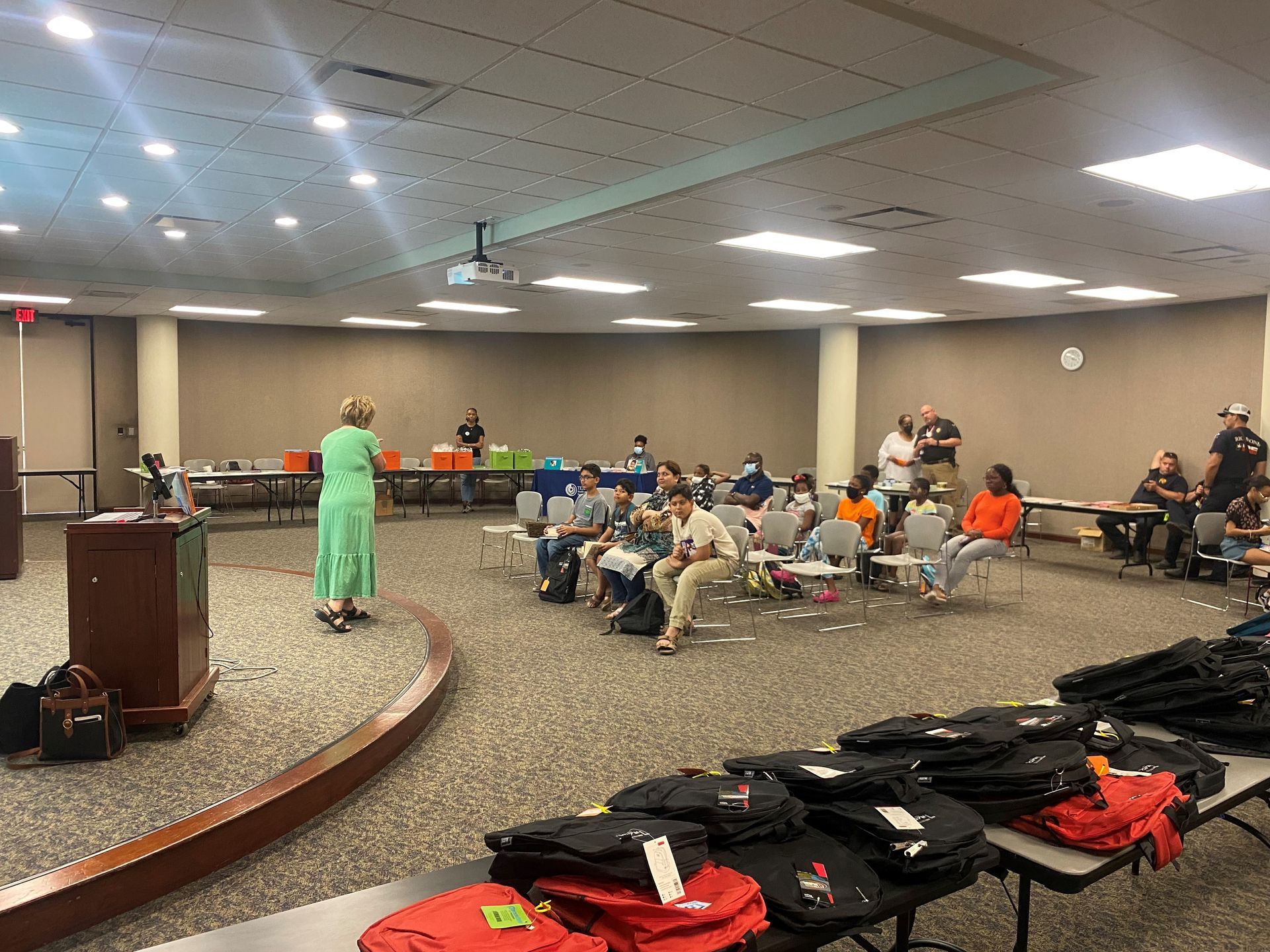 Woman speaking at a podium in a meeting room with attendees and t-shirts on tables.